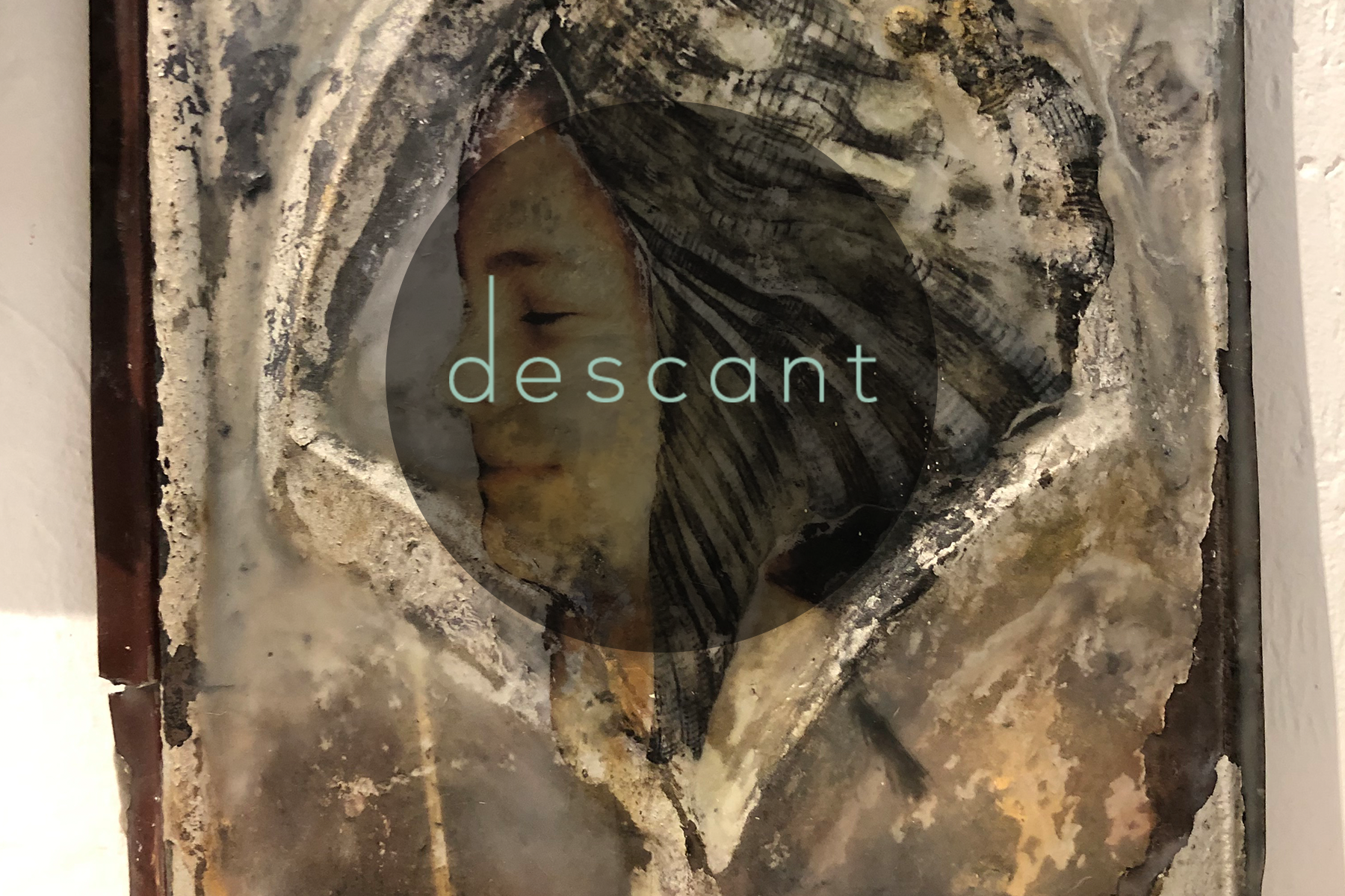 the image shows a wood carving/paining of a girl with black hair smiling while only showing the left half of her face. There is a gray cirlce over the image and the word descant is atop the circle in teal letters