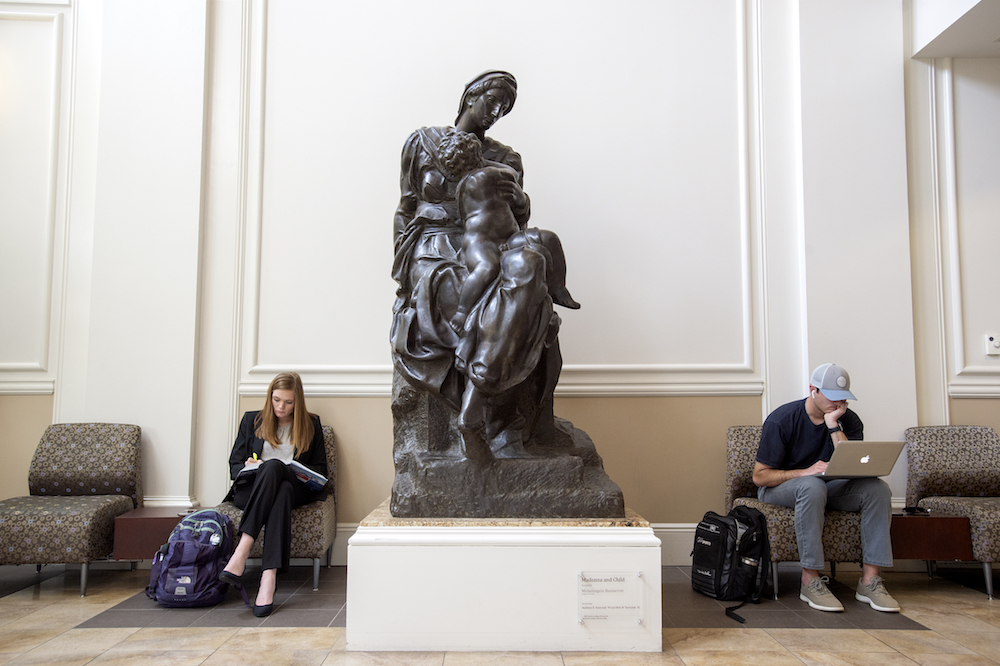 Two students sit near a statue in the lobby of Scharbauer Hall