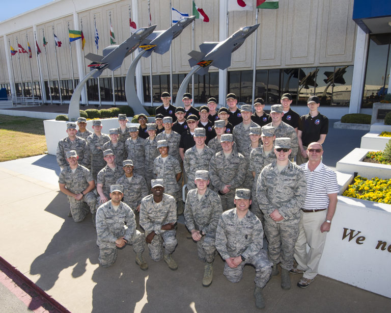 A group of Air Force cadets gathered in front of a sculpture of fighter jets
