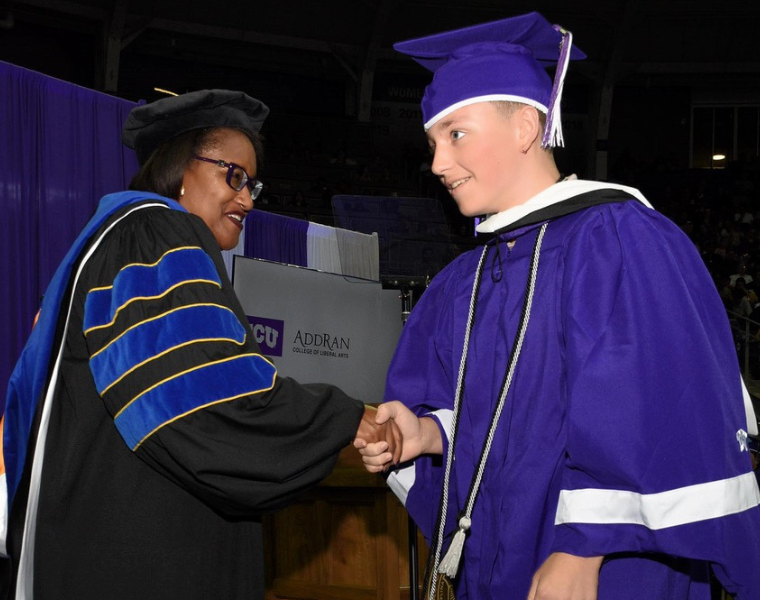 Andrew Stewart shaking AddRan College of Liberal Arts Dean Sonja Watson's hand on the commencement stage.