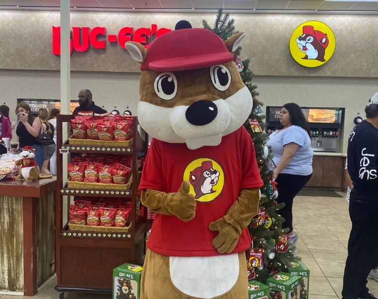 A person in a Buc-ee's beaver costume wearing a red cap and shirt stands in the store. The logo 