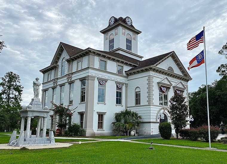 Three-quarter view of a Georgia courthouse, with a statue the American and Georgia state flags in the foreground