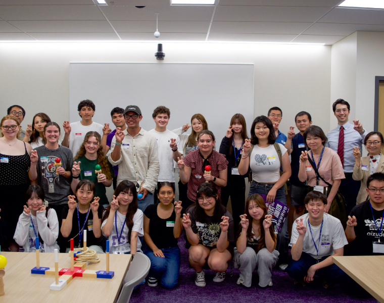 A group of students stand together in a room, smiling and holding up their hands in a Go Frogs gesture. 