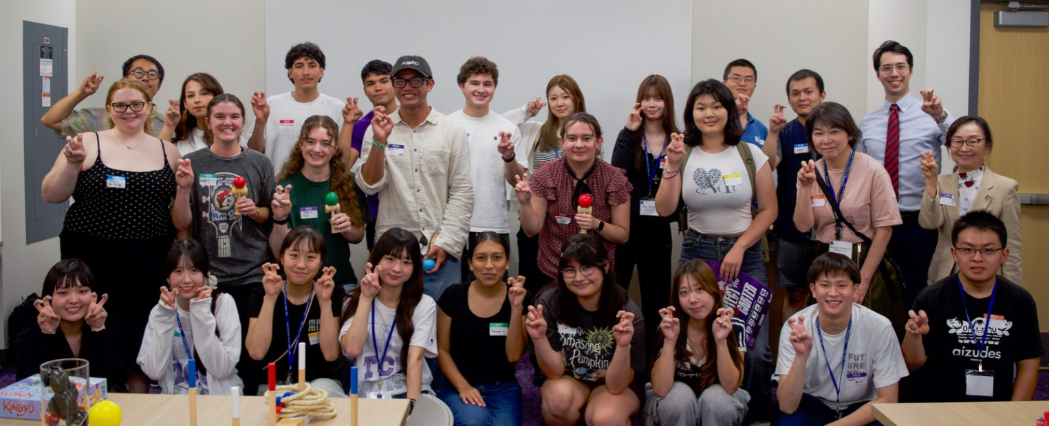 A group of students stand together in a room, smiling and holding up their hands in a Go Frogs gesture. 
